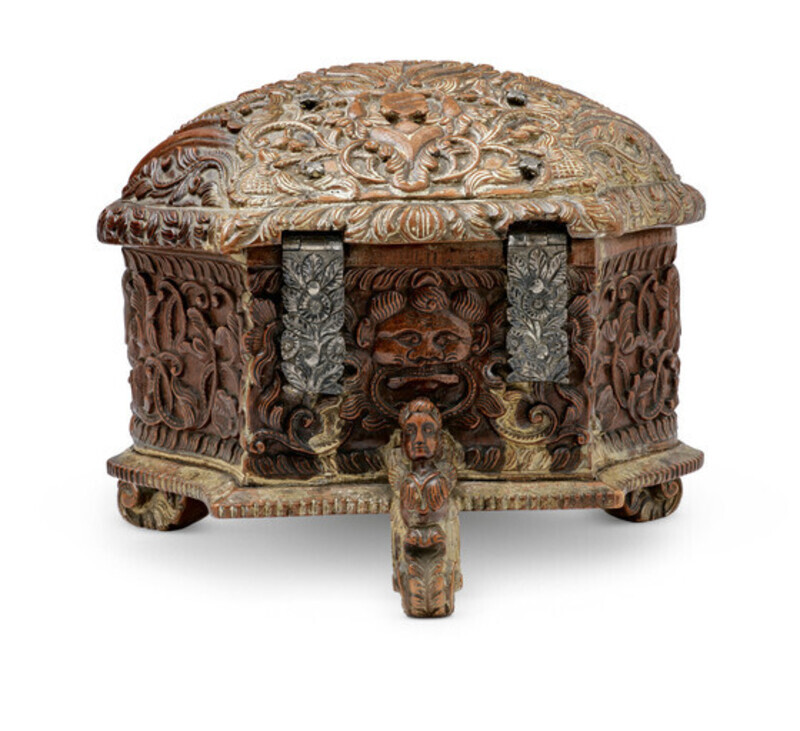 Ornate wooden box in the shape of a shell with detailed carvings, metal lock, and three small feet shaped like mythical creatures, photographed from behind on a white background.