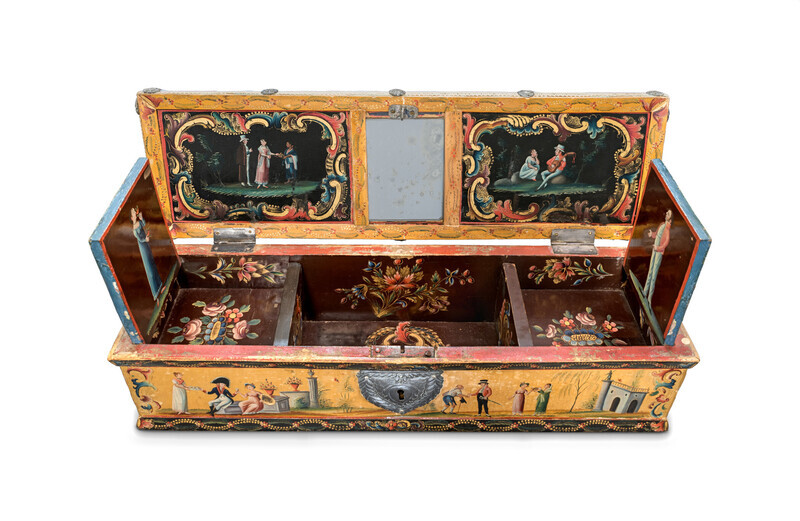 An ornate, rectangular wooden box with hand-painted scenes in imitation lacquer, a central lock, two opened small interior compartments, and a mirror on the inside of the lid photographed on a white background. The hand-painted scenes depict willow trees, scenes of courtship, charity, battle, and portraits of fashionable men and women. 