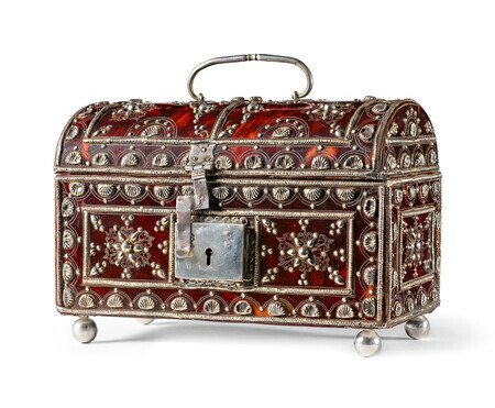 Casket made of tortoiseshell with a silver lock and handle, silver decoration, and silver ball feet. Silver decoration takes the form of seashells and abstract geometric patterns. Photographed on a white background.
